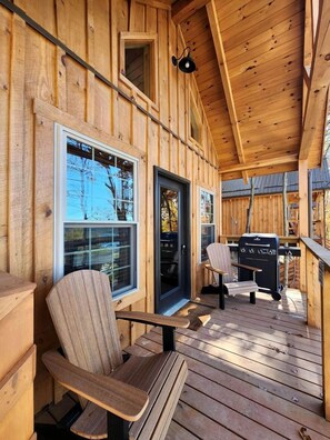 Una terraza de madera con una parrilla, sillas, una puerta y ventanas.
