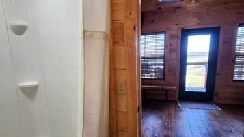 A wooden interior with a shower, a door leading to a room with a view, and a window with blinds.