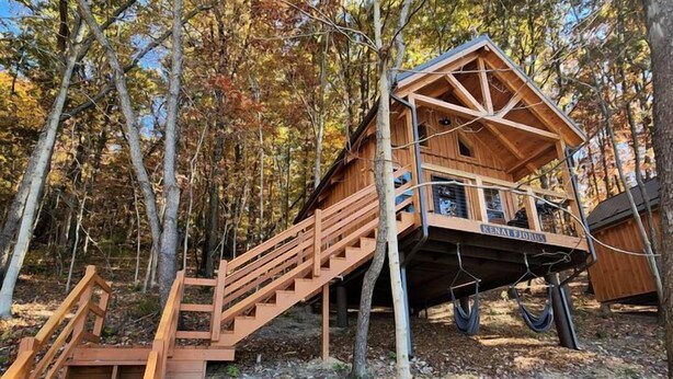 Eine Holzhütte mit einer Treppe, die zu einer Terrasse führt, umgeben von Bäumen.