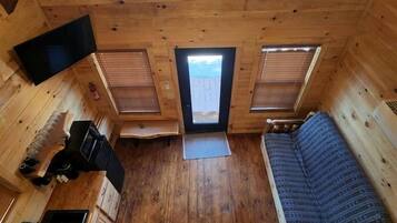 A cabin with a loft bedroom, a kitchenette, and a large window.