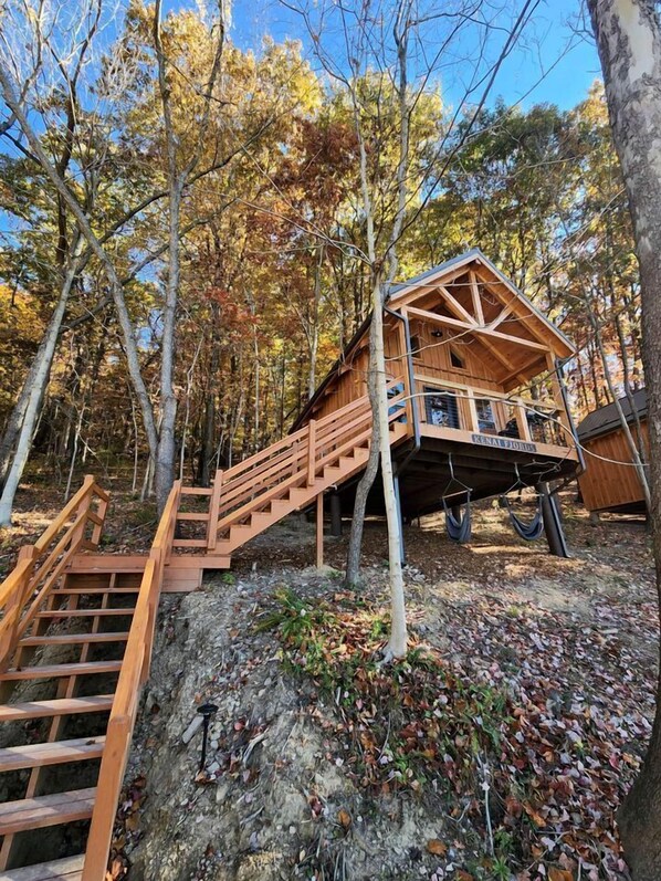 Une cabane en bois avec un escalier menant à une terrasse, entourée d’arbres.