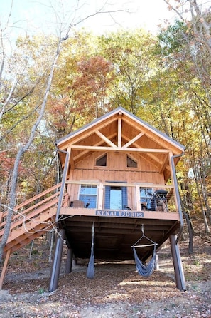Une cabane en bois dotée d’un balcon, d’un escalier et d’un hamac suspendu.