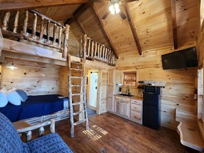 A cabin interior with a loft bedroom, a kitchen with a microwave, and a wooden staircase.