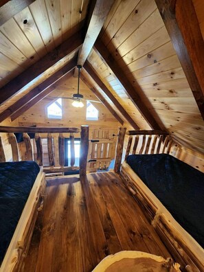 Une chambre à coucher aménagée dans les combles, avec un plafond en pente, deux fenêtres et une poutre en bois centrale.