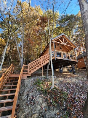 Eine Holzhütte mit einer Treppe, die zu einer Terrasse führt, umgeben von Bäumen.