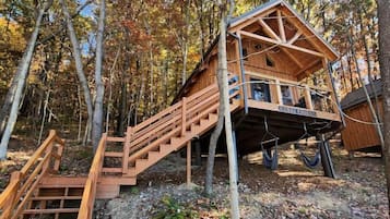 A wooden cabin with a staircase leading up to a deck, surrounded by trees.