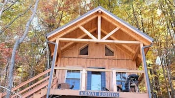 A wooden cabin with a balcony, a staircase, and a hanging hammock.