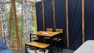 Ein Zimmer mit Holztisch und -stühlen, einem Bett und einem Fenster mit Vorhängen.