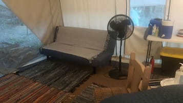 A tent interior with a sofa, a fan, a small table with items, and a window.