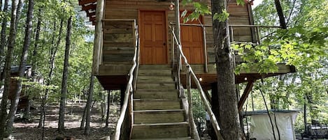 Una cabaña de madera con una escalera que conduce a una puerta, rodeada de árboles.
