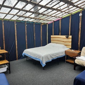 Quarto com cama, mesa de cabeceira de madeira, cadeira, escrivaninha e janela com moldura de bambu.