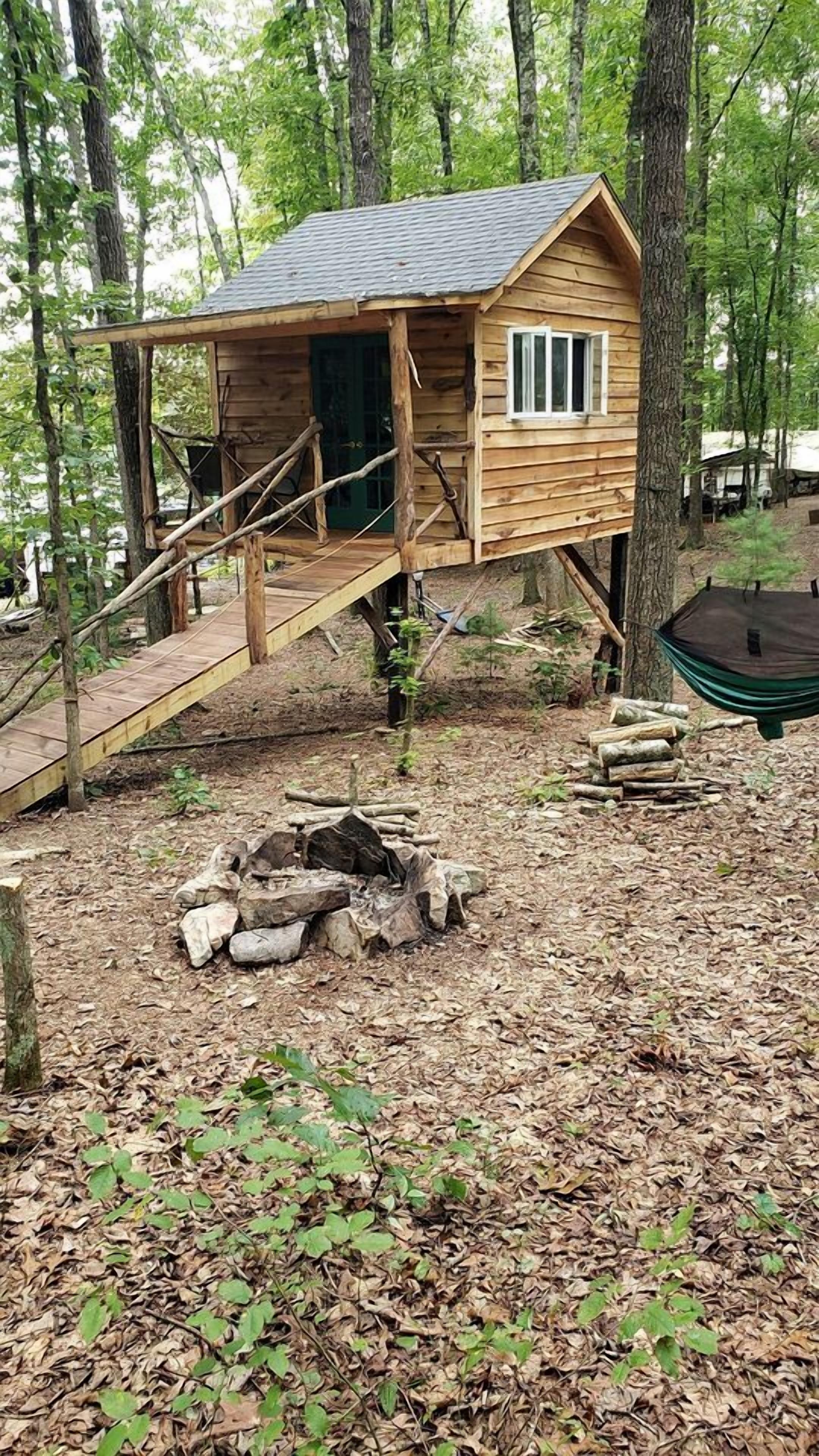 A wooden treehouse with a staircase, a fire pit, and a hammock.