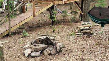 A wooden treehouse with a staircase, a fire pit, and a hammock.