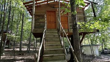 A wooden cabin with a staircase leading to a door, surrounded by trees.
