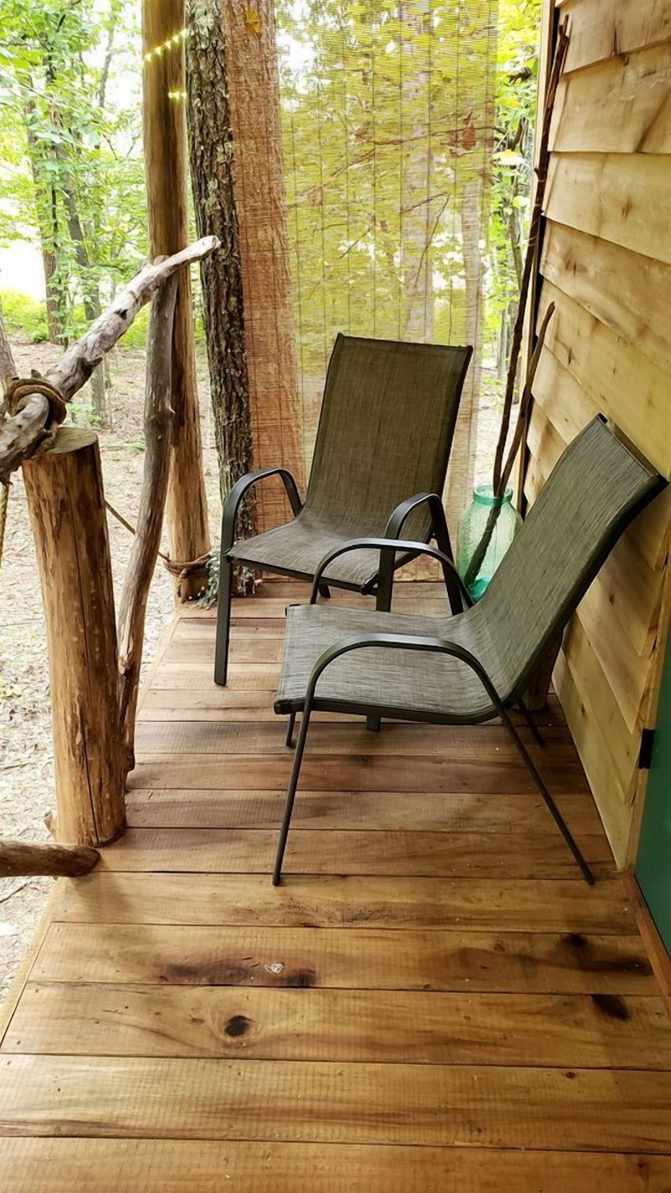 A wooden deck with two metal chairs and a tree trunk.