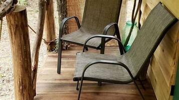 A wooden deck with two metal chairs and a tree trunk.
