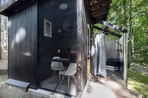 A small cabin with a single table and two chairs, a shower area, and a wooden deck.
