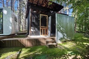Pieni mökki, jossa on puinen terassi, ovi ja ikkuna.