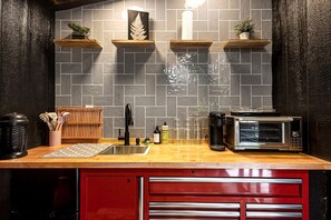 Una cocina con salpicadero de azulejos, estantes de madera, un fregadero, un microondas y un armario rojo.
