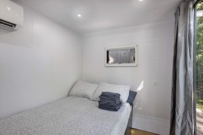 A bedroom with a bed, a window, and an air conditioning unit.
