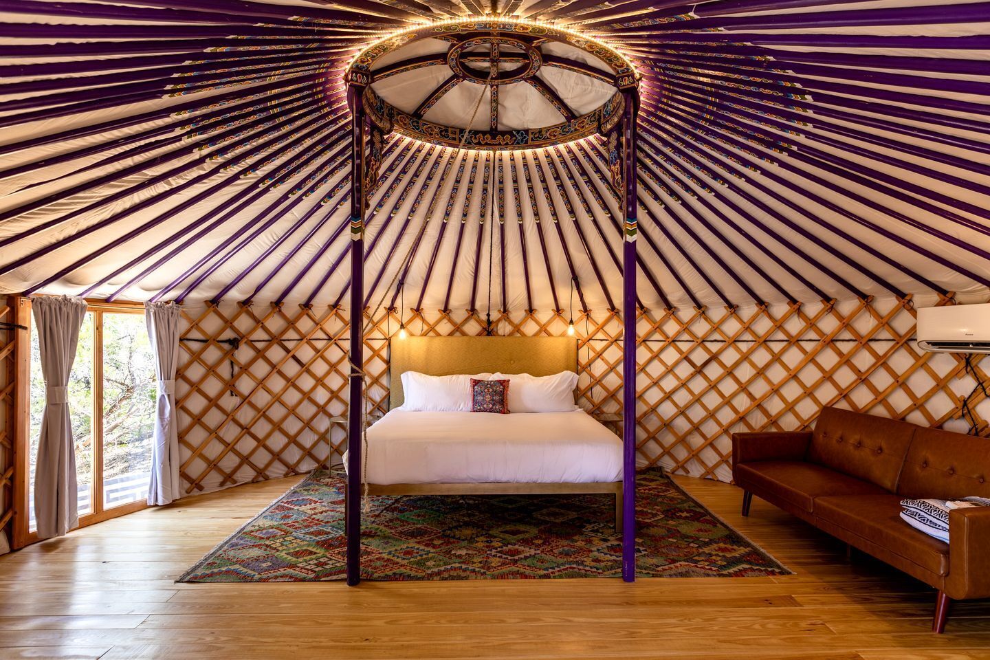 A room with a bed, a sofa, a patterned rug, and a wooden floor.