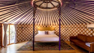 A room with a bed, a sofa, a patterned rug, and a wooden floor.