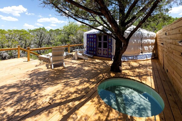 Una terraza de madera con un jacuzzi, una zona de estar cubierta y un árbol.