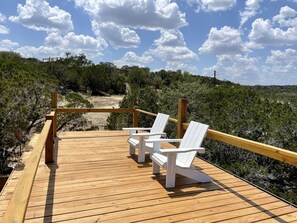 A wooden deck with white chairs, overlooking a beach with trees and a clear sky.