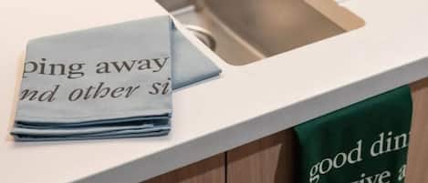 Una encimera de cocina con una toalla que dice “ping away y otras sí” y una toalla verde con el texto “buena comida perdona a”.