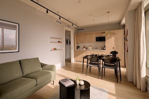Un salon moderne comprenant un canapé, une table à manger avec des chaises, un coin cuisine avec des meubles en bois et une grande fenêtre agrémentée de rideaux.