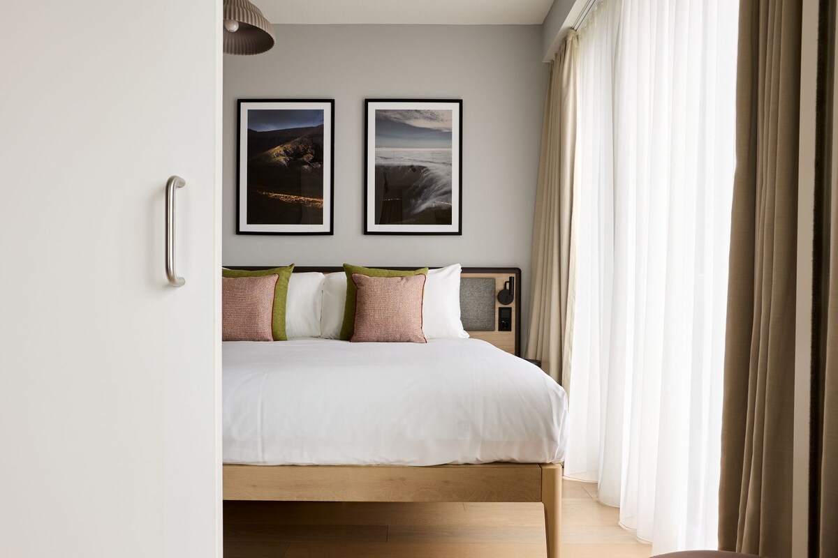 Een slaapkamer met een houten bed, witte beddengoed en twee ingelijste foto’s aan de muur.