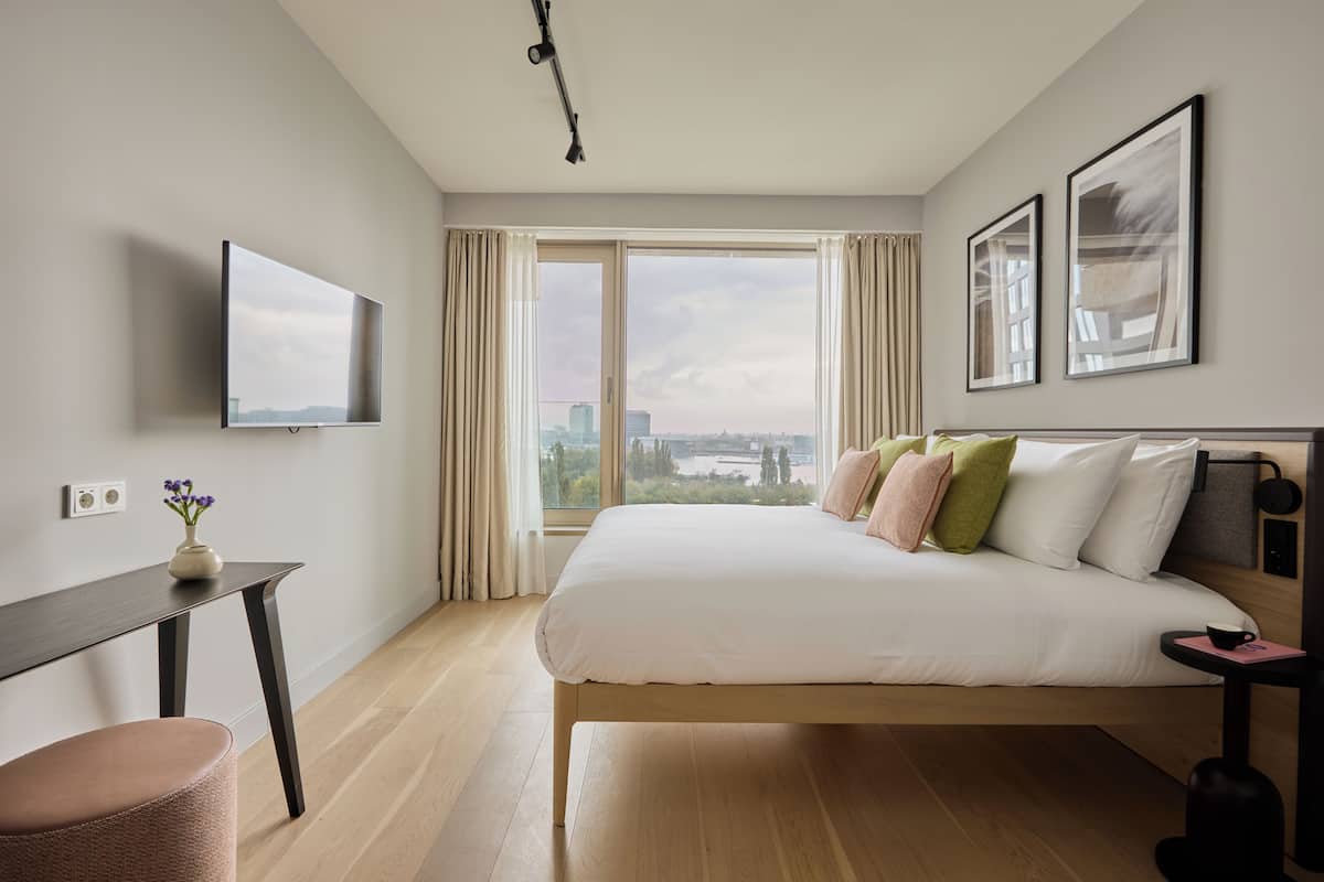 Een moderne hotelkamer met een groot bed, een bureau, een stoel en een aan de muur bevestigde televisie.