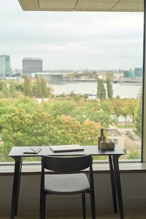 Une chambre avec vue sur une rivière et sur le paysage urbain, un bureau avec une chaise et un vase rempli de fleurs.