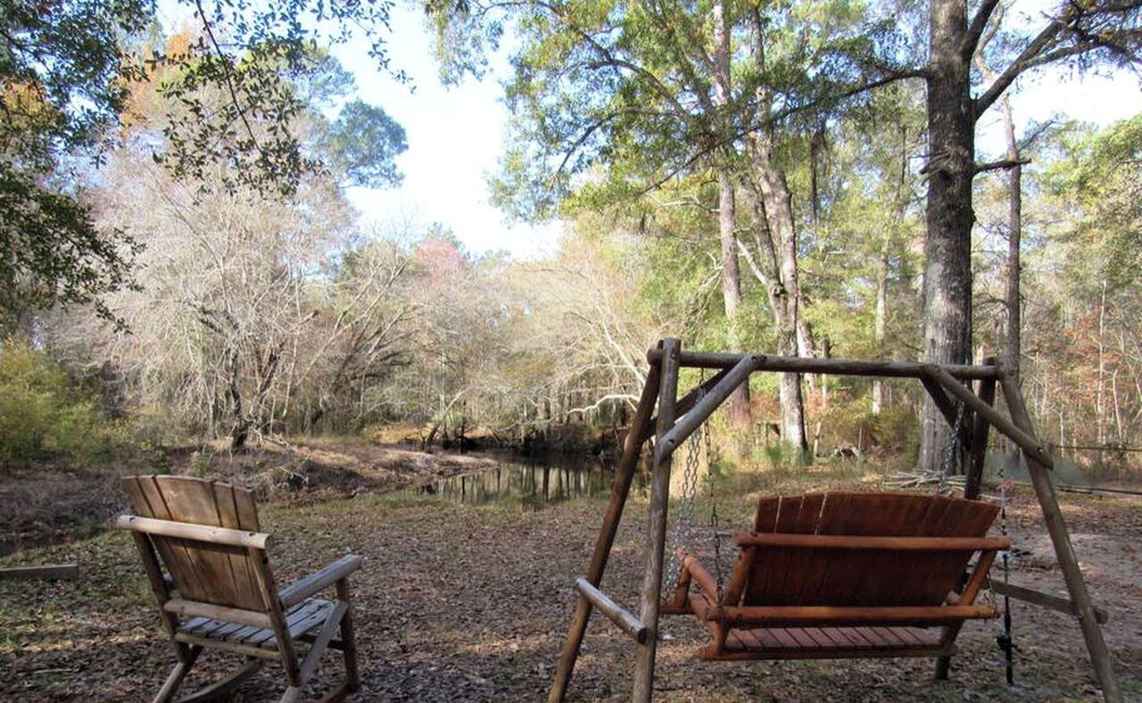 A wooden swing set in a wooded area with a bench and a small pond.