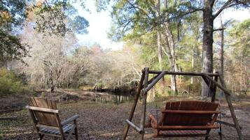 A wooden swing set in a wooded area with a bench and a small pond.