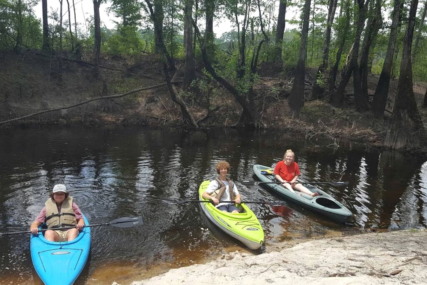 Three kayaks on a calm river surrounded by trees.