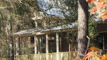 A wooden cabin with a balcony, surrounded by trees and foliage.