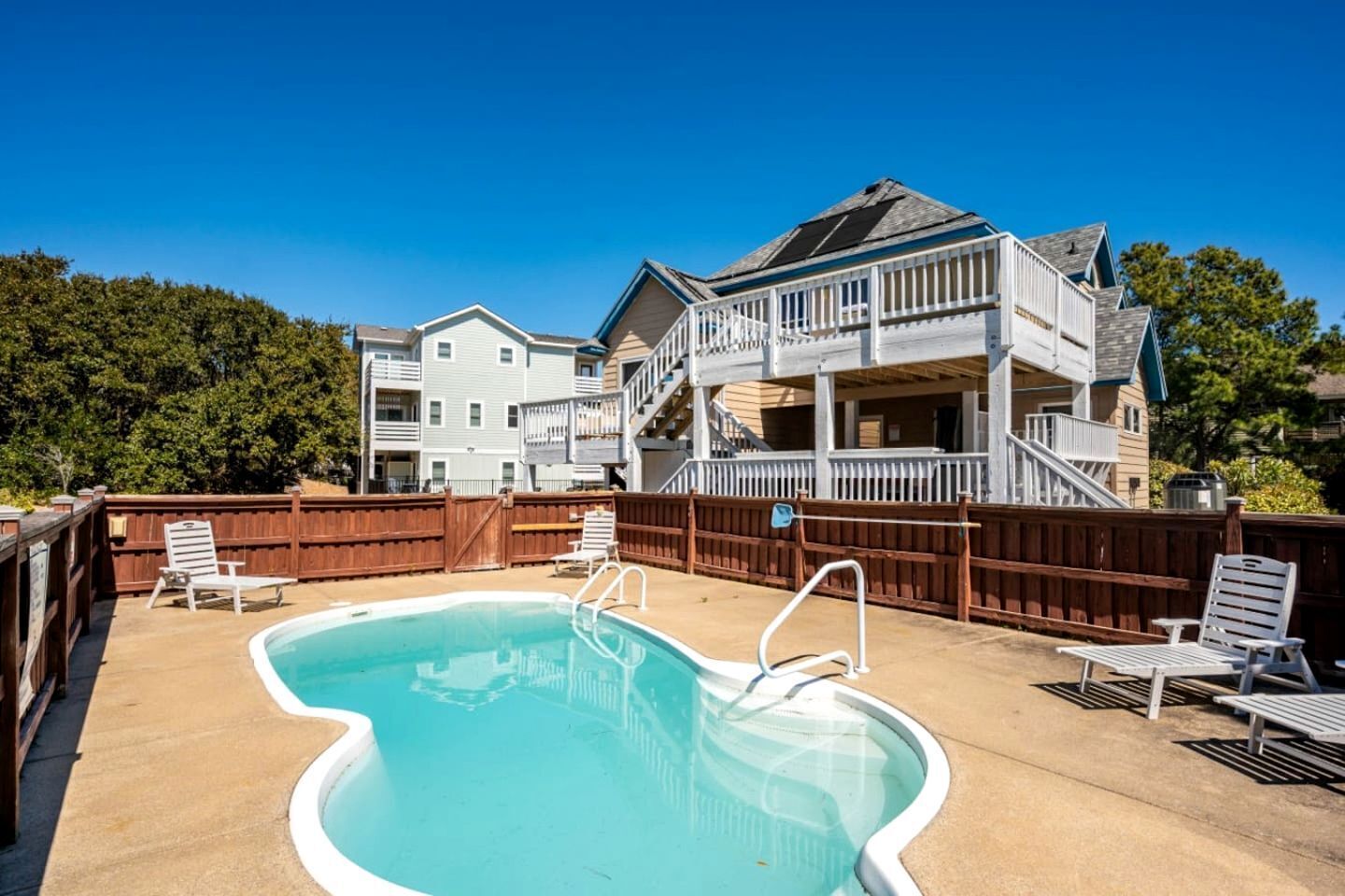 A residential setting with a swimming pool, outdoor furniture, and a two-story house with a balcony.