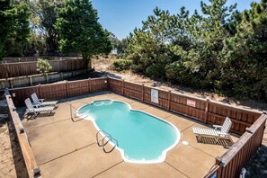 A backyard with a swimming pool, wooden deck, and lounge chairs.