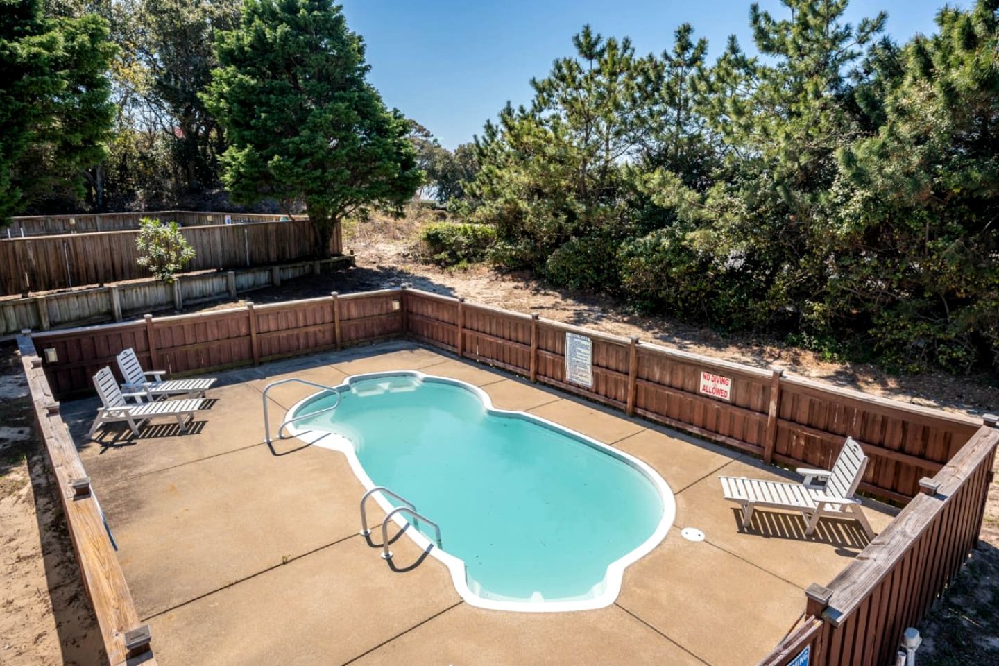 Un jardin avec une piscine, une terrasse en bois et des chaises longues.