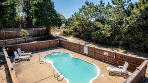 A backyard with a swimming pool, wooden deck, and lounge chairs.