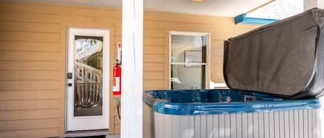 A covered porch with a hot tub, a door, and a fire extinguisher.