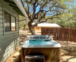 A hot tub in a backyard with a wooden deck, a tree, and a house in the background.