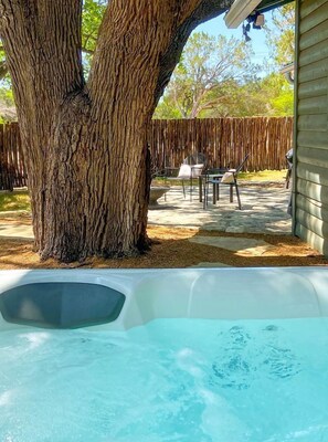 A hot tub under a large tree, outdoor seating area with chairs, and a wooden fence.