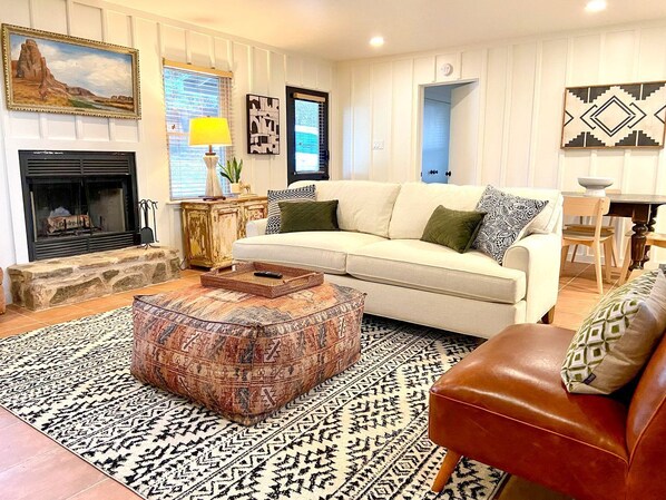 Un salon comprenant un canapé, un pouf, une cheminée et un tapis à motifs.