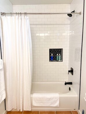 A shower with a curtain, a glass-enclosed showerhead, and a tiled wall.