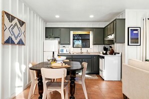 Een moderne keuken met een eethoek, met een centraal kookeiland, witte apparaten en uitzicht op de omgeving.