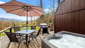 A wooden deck with a hot tub, a table with chairs, and a barbecue grill.