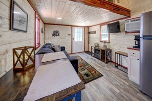 Interior de cabana com piso de madeira, sofá, mesa, televisão e frigorífico.