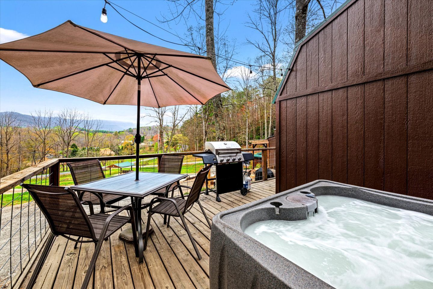 Una terraza de madera con un jacuzzi, una mesa con sillas y una parrilla.